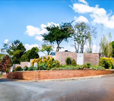 a brick wall next to a street with trees at Rusgerus in Pretoria