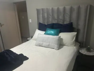 a white bed with blue and white pillows on it at Two Bedrooms in the Capital City in Pretoria