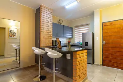 a kitchen with a bar with stools and a refrigerator at The Local house in Midrand