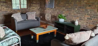 a living room with two chairs and a brick wall at Cottage On Naboom in Marloth Park