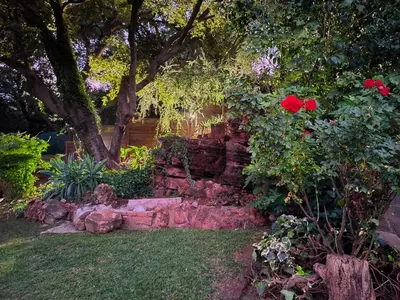 a garden with a stone wall and red roses at Wag-n-Bietjie in Centurion