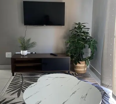 a living room with a tv and a table with plants at Warm, Homely Apartment - 5min Away Menlyn Main in Pretoria