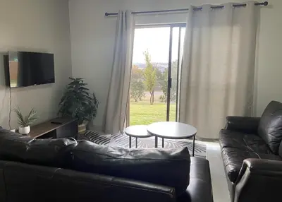 a living room with a couch and a table and a window at Warm, Homely Apartment - 5min Away Menlyn Main in Pretoria