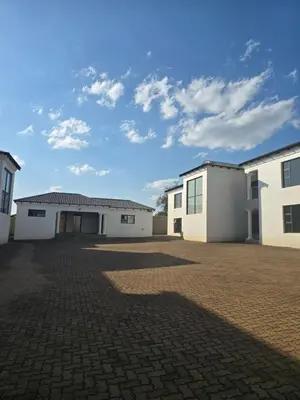 a row of white buildings on a brick parking lot at Limpopo LidoSystem Lodge