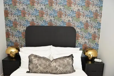 a bedroom with a bed with a black headboard and floral wallpaper at Ellipse Olive and Vine in Midrand