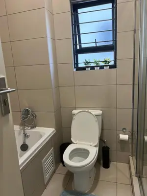 a bathroom with a toilet and a sink and a window at The West End 252 in Midrand