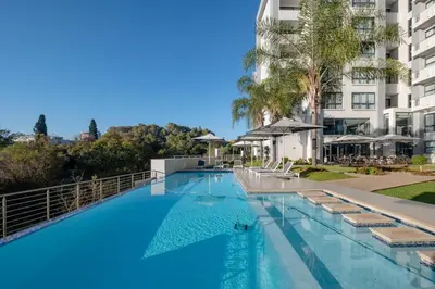 a large swimming pool with chairs and a building at Modern loft at Regency in Pretoria