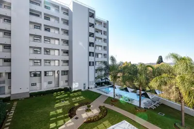 an apartment building with a pool and palm trees at Modern loft at Regency in Pretoria