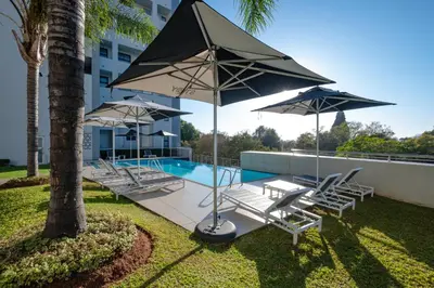 a group of chairs and umbrellas next to a pool at Modern loft at Regency in Pretoria