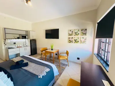 a bedroom with a bed and a table and a kitchen at Promenade Place Nelspruit in Nelspruit