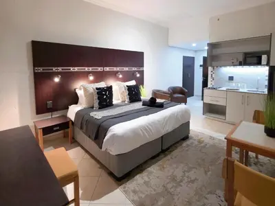 a bedroom with a large bed and a kitchen at Promenade Place Nelspruit in Nelspruit