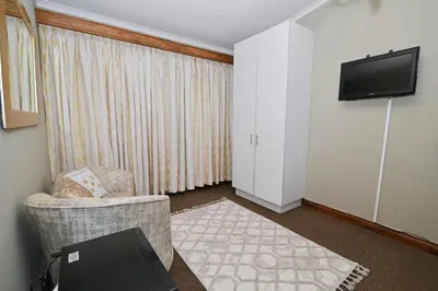 a living room with a chair and a tv on a wall at Morning Star Guest House in Kempton Park