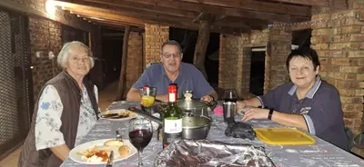 three people sitting at a table with food and wine at Martys Place in Marloth Park
