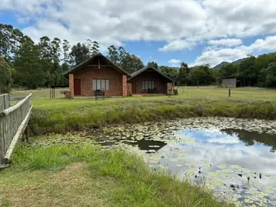 a house in a field next to a pond at Harnham Mountain Lodge in Elsteg