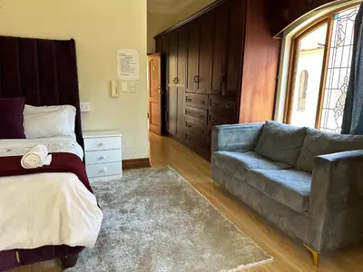 a bedroom with a bed and a couch and a window at Crown Guesthouse-Waterkloof in Pretoria
