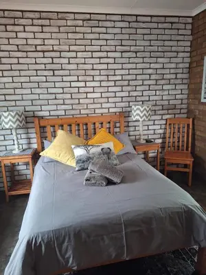 a bedroom with a bed with two chairs and a brick wall at Oppieplaas in Alldays