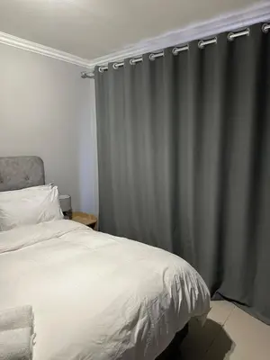 a bedroom with a bed and a gray curtain at The Olive Nook 2-Bed in Midrand in Midrand