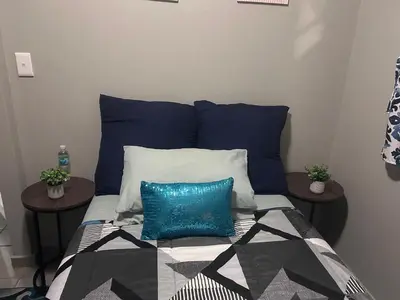 a bed with blue and white pillows and two tables at Peaceful Cute Apartment in Pretoria