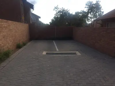 a parking lot with a brick wall and a grate at Lovely 2 Bedroom Townhouse with private garden in Centurion