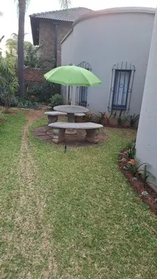 a picnic table with a green umbrella in a yard at Casa Maya in Pretoria