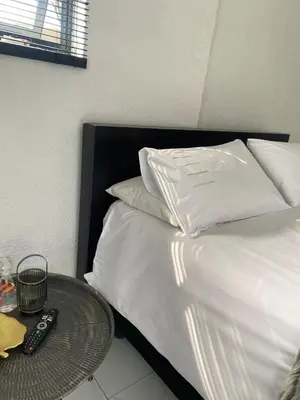 a bed with white sheets and pillows next to a table at Lakeside Studio Sleeps max 2 in Benoni