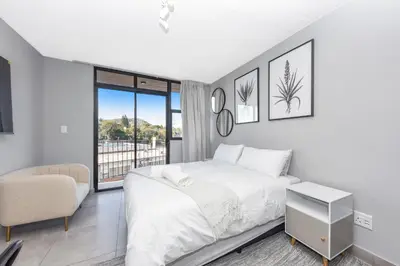 a white bedroom with a bed and a chair at Circa Lynwood Accommodation in Pretoria