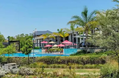 a resort with a swimming pool with red umbrellas at #AlimamaSpaces The Rob's Polofields in Midrand
