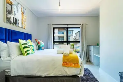 a bedroom with a large white bed with colorful pillows at #AlimamaSpaces The Rob's Polofields in Midrand