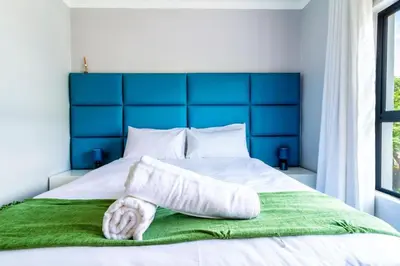 a bed with a blue headboard and a green blanket at AlimamaSpaces Farais Whisken Apartment in Midrand