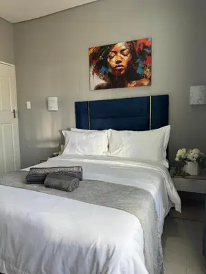 a bedroom with a large white bed with a painting on the wall at Glowti Event & Guest House in Centurion