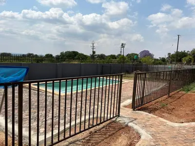 a metal fence around a swimming pool in a park at Glowti Event & Guest House in Centurion
