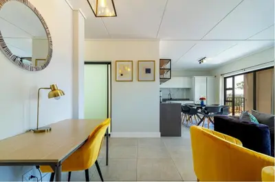 a dining room and living room with a table and yellow chairs at #AlimamaSpaces Jay's Polofields in Midrand