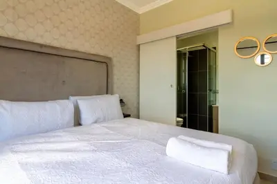 a bedroom with a large white bed and a mirror at #AlimamaSpaces The Rob's Kyalami Woods in Midrand