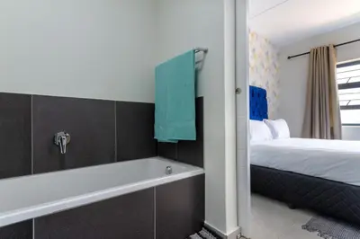 a bathroom with a bath tub next to a bed at #AlimamaSpaces The Chelsea Kyalami Woods in Midrand