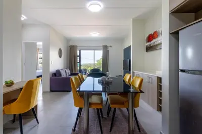 a kitchen and dining room with a table and yellow chairs at #AlimamaSpaces The Chelsea Kyalami Woods in Midrand