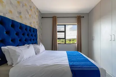 a bedroom with a large bed with a blue headboard at #AlimamaSpaces The Bob's Kyalami Woods in Midrand