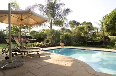 a swimming pool with two chairs and an umbrella at Royal Ridge Guesthouse in Pretoria