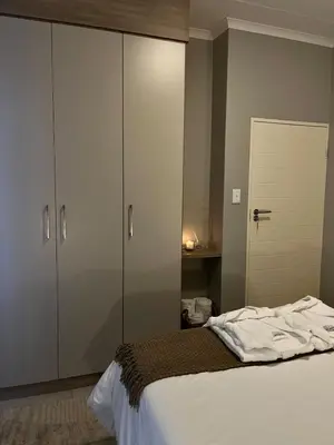 a bedroom with a bed with white sheets and cabinets at Kurhula Suite Apartment in midrand in Midrand