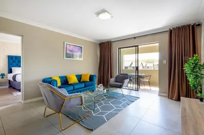 a living room with a blue couch and a glass table at Alimamaspaces The Mansons Riverbend Midrand in Midrand