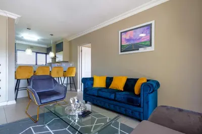a living room with a blue couch and yellow pillows at Alimamaspaces The Mansons Riverbend Midrand in Midrand