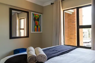 a bedroom with a bed with rolled towels on it at Alimamaspaces The Mansons Riverbend Midrand in Midrand