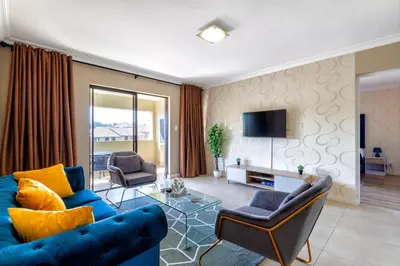 a living room with a blue couch and chairs at Alimamaspaces The Mansons Riverbend Midrand in Midrand
