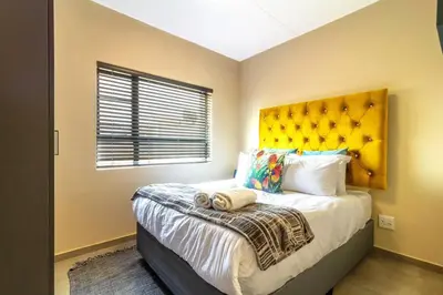 a bedroom with a large bed with a yellow headboard at AlimamaSpaces Bonitos Waterfall Ridge in Midrand