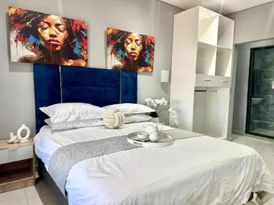 a bedroom with a large white bed with paintings on the wall at Glow Events &Guest House in Centurion