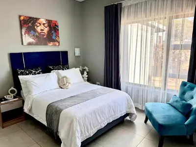 a bedroom with a large bed and a blue chair at Glow Events & Guest House in Centurion