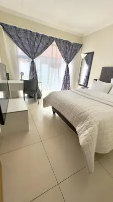 a bedroom with a bed and a desk and a window at Prospect Guest House in Pretoria