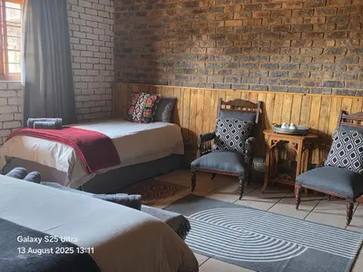 a bedroom with two beds and two chairs and a brick wall at Veldjie Huis in Temba