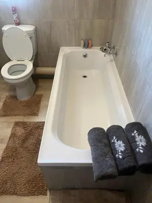 a bathroom with a bath tub with two towels and a toilet at Modern Style Apartments, An Escape From The City in Pretoria