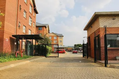 an empty street next to a brick building with a gate at Modern Style Apartments, An Escape From The City in Pretoria