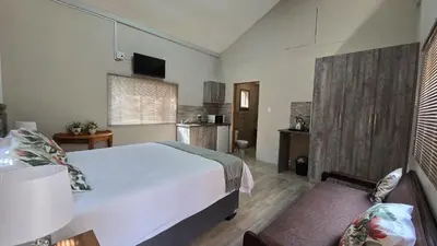 a bedroom with a large white bed and a kitchen at The Magalies Nest - Self Catering Accomodation in Hartbeespoort